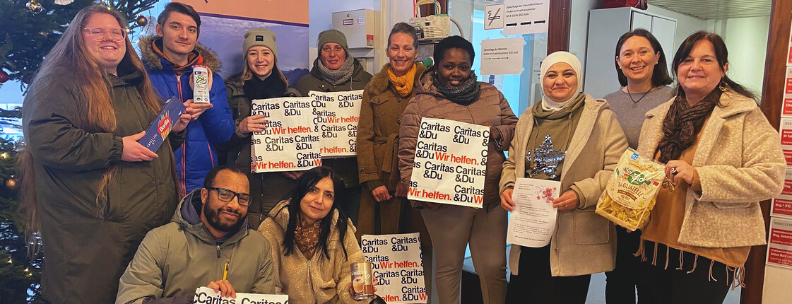 Eine Gruppe Erwachsener steht nebeneinander und hält Caritas Säcke in der Hand. Links ist ein Christbaum zu sehen.