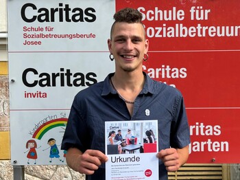 Junger Mann lächelt und hält eine Urkunde in die Kamera