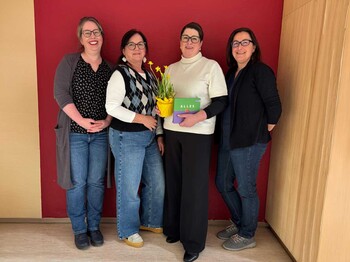 Vier Frauen stehen beisammen und zwei halten einen Blumenschmuck und Schokolade in den Händen.