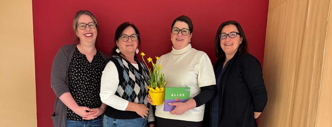 Vier Frauen stehen beisammen und zwei halten einen Blumenschmuck und Schokolade in den Händen.