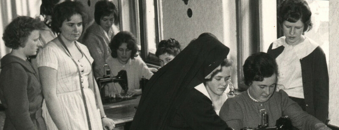 Eine Nonne zeigt jungen Frauen das Nähen an einer Nähmaschine